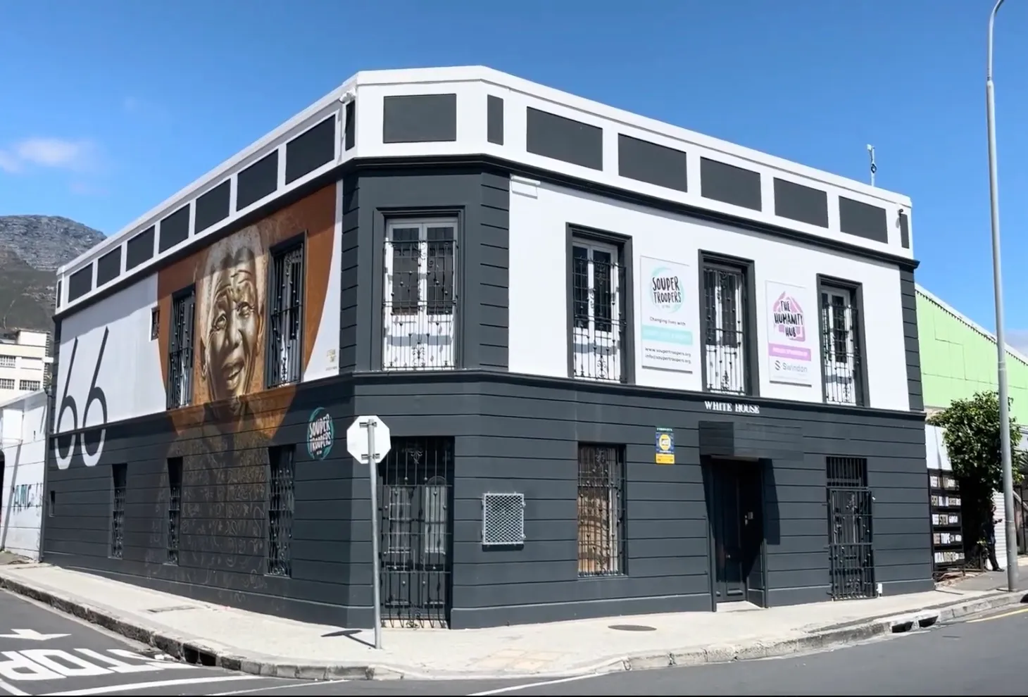 The Humanity Hub at 66 Newmarket Street - a grey and white corner building with a large 66 and a mural of Nelson Mandela on its side wall, Table Mountain behind it.