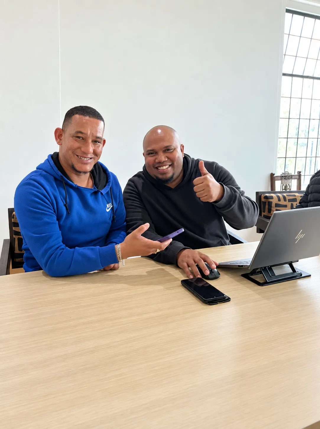 Two smiling visitors at a table at The Humanity Hub, one giving a thumbs up